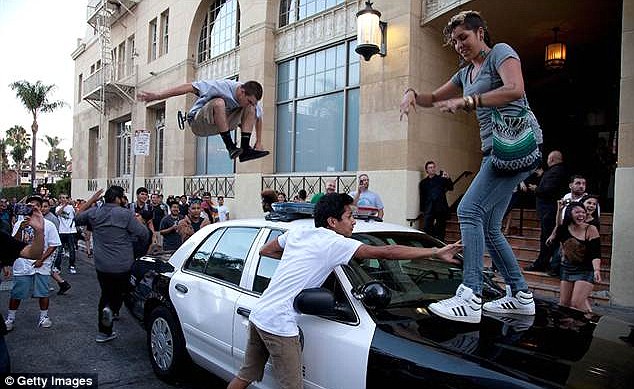 Over-zealous revellers jump up and down on a police car after crowds got out of hand outside a Hollywood film première