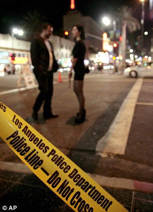 A couple waits at the intersection of Hollywood Boulevard and Highland Avenue after an unruly crowd trying to attend an Electric Daisy Carnival concert film threw rocks and bottles at police cars in Los Angeles, Wednesday, July 27